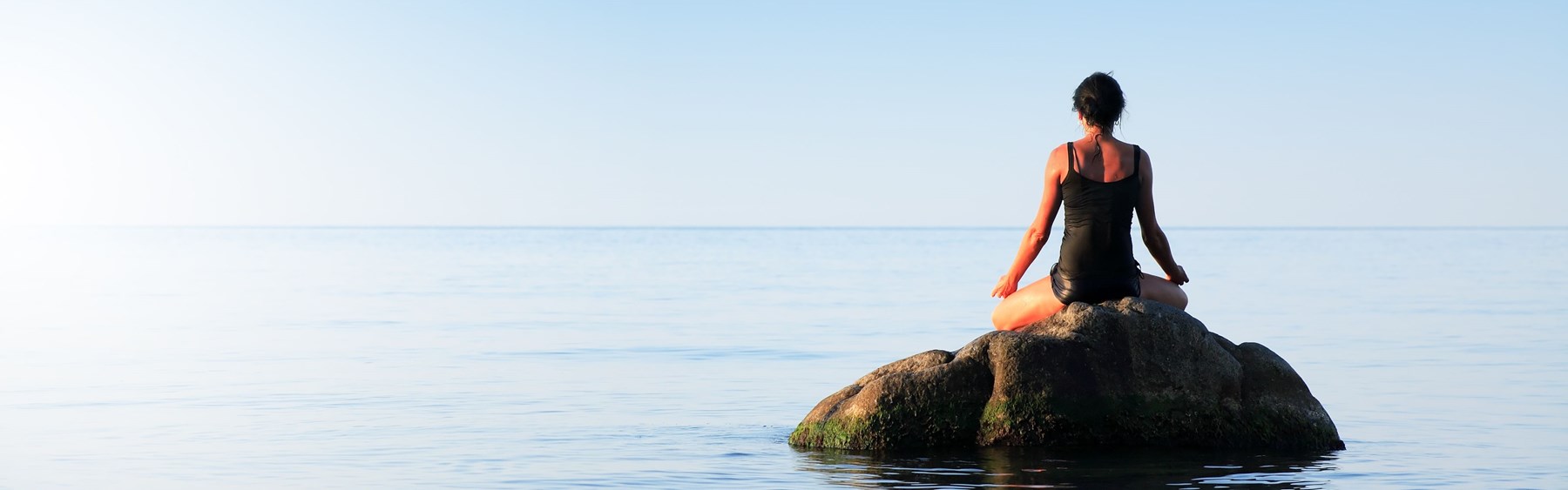 Kvinde sidder på sten og meditere i vandet